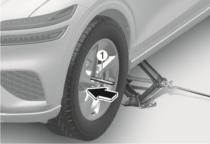 2025 Genesis GV70 centering pin installation image. A centering pin (1) is inserted into a wheel bolt hole on the hub, highlighted by a black arrow pointing towards it. The vehicle is supported by a jack. Explains the function of inserting the centering pin to align the wheel during tire replacement.