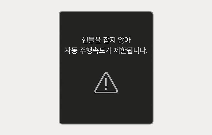 2025 제네시스 GV70 고속도로 주행 보조 주행속도 제한 경고 이미지입니다. 검은색 배경의 클러스터 화면 중앙에 삼각형 모양의 느낌표 경고 아이콘이 있고, 상단에 '핸들을 잡지 않아 자동 주행속도가 제한됩니다.'라는 흰색 안내 문구가 표시되어 있습니다. 핸즈오프 상태가 지속되어 주행 속도가 제한됨을 알리는 기능을 설명합니다.